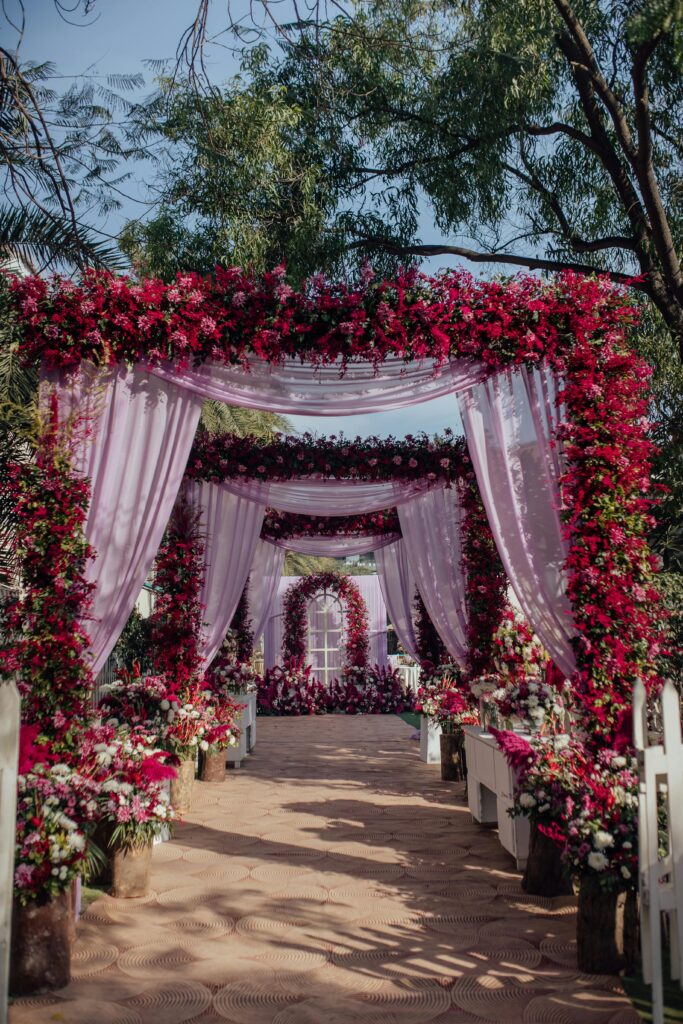 Elegant outdoor wedding arch adorned with vibrant pink and red flowers, creating a romantic ambiance.